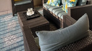 A balcony with wicker furniture, a fire alarm, a clock, and a painting of a beach.