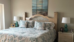 A bedroom with a bed, two nightstands, a ceiling fan, and a painting on the wall.