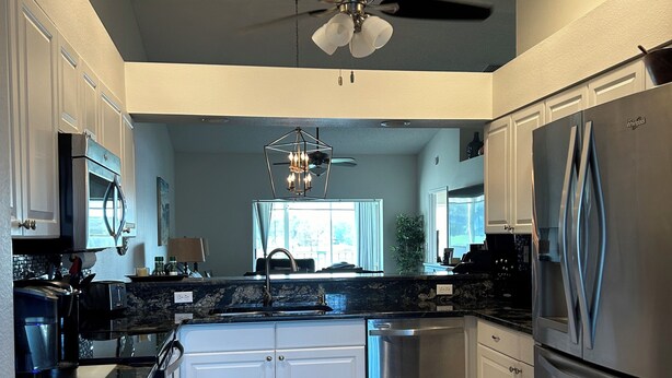 A modern kitchen with white cabinets, stainless steel appliances, a central island, and a ceiling fan.