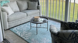 A living room with a grey sofa, a round coffee table, and a large window offering a view of a golf course.