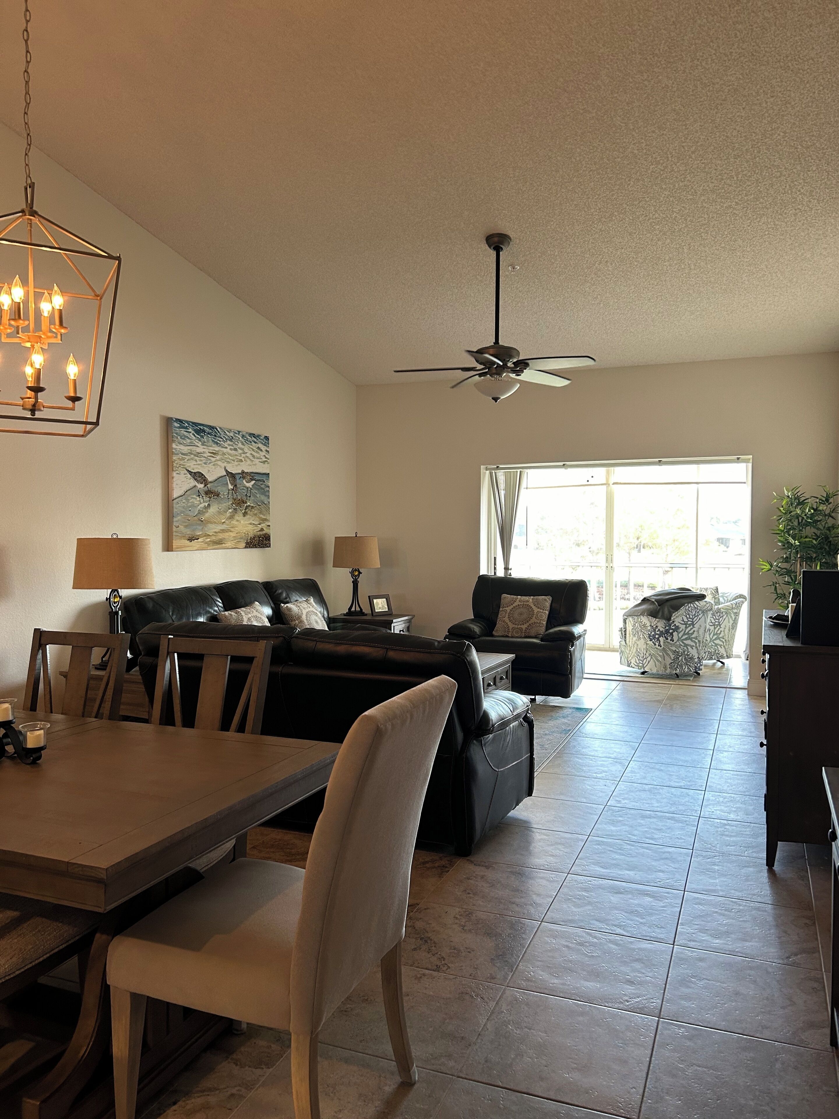 A spacious living room with a dining area, a ceiling fan, and a large window with curtains.