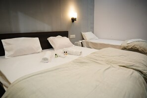 A hotel room with two beds, each with white linens and pillows. There is a wall-mounted light fixture above the beds. - Maha Kumbh Mandapam  (Karchana)