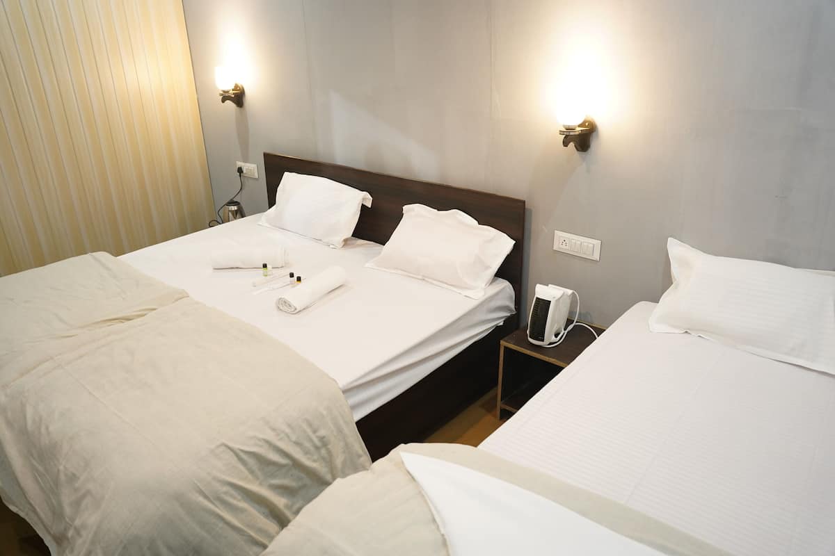 Ett hotellrum med två sängar, båda med vita sängkläder och kuddar, ett nattduksbord med en lampa och väggmonterade lampor.