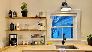 Ett modernt kök med trähyllor, en kaffemaskin och ett fönster med utsikt över ett hus.