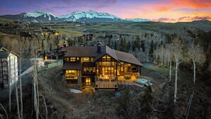 A large, modern two-story house with a spacious outdoor area, including a patio and a hot tub, surrounded by a mountainous landscape. - Telluride Ridge / Hot Tub, Fire Pit & Mountain Views (Mountain Village)