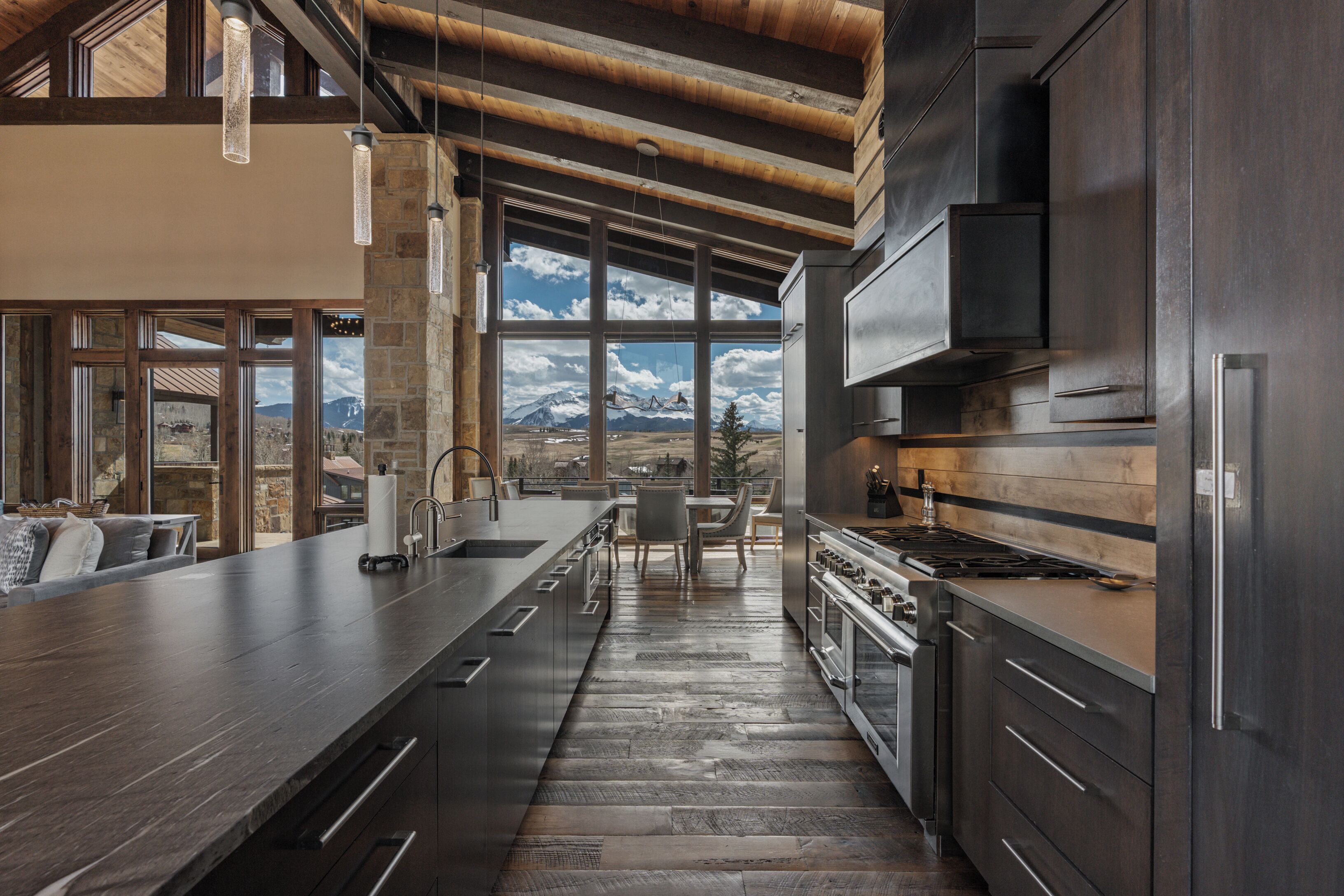 Une cuisine moderne dotée d’un grand îlot central, d’appareils électroménagers en acier inoxydable et offrant une vue sur les montagnes grâce à de grandes fenêtres.