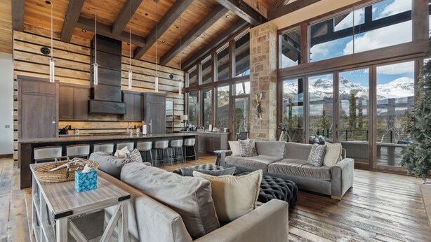 A spacious living area with a large sofa set, a wooden coffee table, and a kitchen area with a stone accent wall. - Telluride Ridge / Hot Tub, Fire Pit & Mountain Views (Mountain Village)