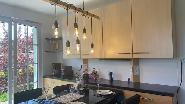 A modern kitchen with wooden cabinets, a black countertop, and hanging light fixtures. - Lovely 3-star country house, ideal for a family. (LEUTENHEIM)