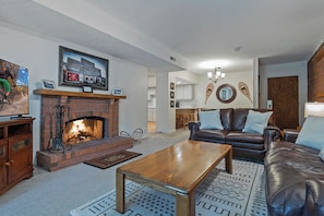 A living room with a fireplace, leather sofa, coffee table, and a mounted picture.