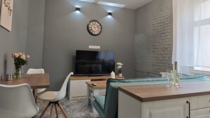 Una sala de estar moderna con un televisor de pantalla plana, una mesa de comedor con sillas, un sofá y una pequeña área de cocina con una cafetera.