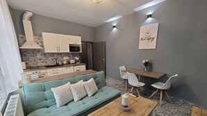 Un espacio habitable compacto con sofá, mesa de comedor y sillas, una kitchenette y un elemento decorativo en la pared.