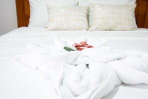 Un lit bien fait, avec un peignoir blanc et une rose posée dessus.