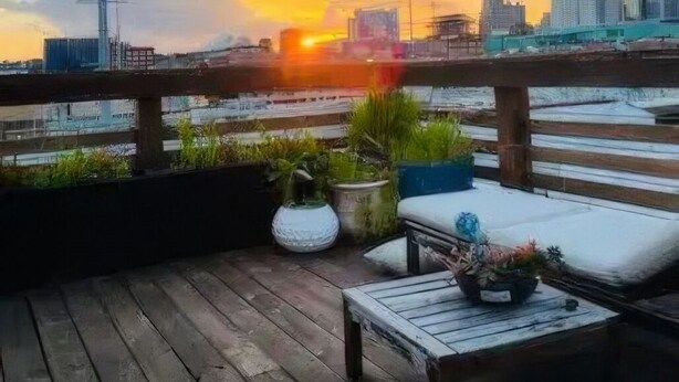 Eine Holzterrasse mit Bank und Pflanzkübeln, mit Blick auf eine Skyline in der Abendsonne.