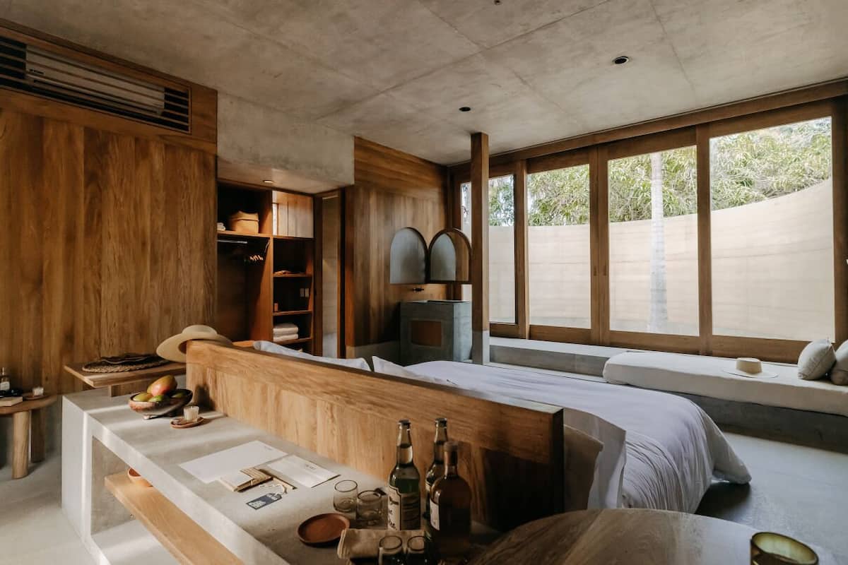 A modern room with a wooden bench, a small table with bottles, and a window with a view.