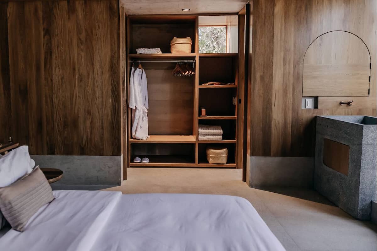 A bedroom with a wooden wardrobe, a bed, and a stone sink.