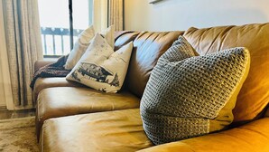 A brown leather sofa with patterned cushions and a blanket.