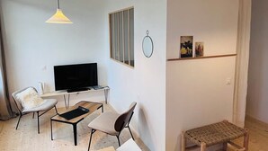 Un salon moderne doté d’un téléviseur à écran plat, de deux fauteuils, d’une petite table, d’un luminaire suspendu et d’un banc en bois.
