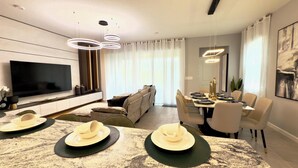 A modern living room with a flat-screen TV, a sofa, and a dining area with a table set for four. - Brand New Charming Home at Solara Resort (Kissimmee)