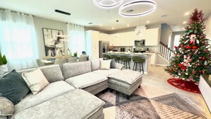 A modern living room with a sectional sofa, a dining area, a kitchen, and a Christmas tree. - Brand New Charming Home at Solara Resort (Kissimmee)