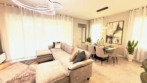 A living room with a sectional sofa, dining table with chairs, and a dining area. - Brand New Charming Home at Solara Resort (Kissimmee)