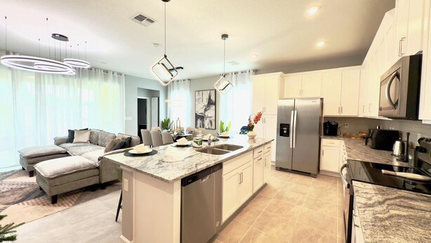 A modern kitchen with a central island, stainless steel appliances, and a dining area with a sofa and chairs. - Brand New Charming Home at Solara Resort (Kissimmee)