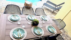 A wooden dining table set for six with matching plates, cutlery, and glasses, surrounded by black wire chairs. - Brand New Charming Home at Solara Resort (Kissimmee)