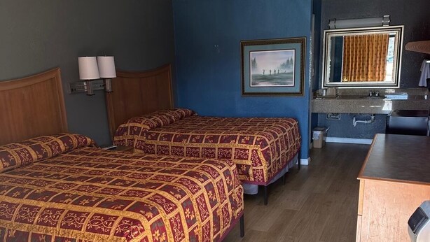 Een hotelkamer met twee bedden, een bureau, een badkamer en een ingelijst foto aan de muur.