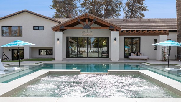 Una casa moderna con piscina, mobiliario exterior y un patio cubierto.
