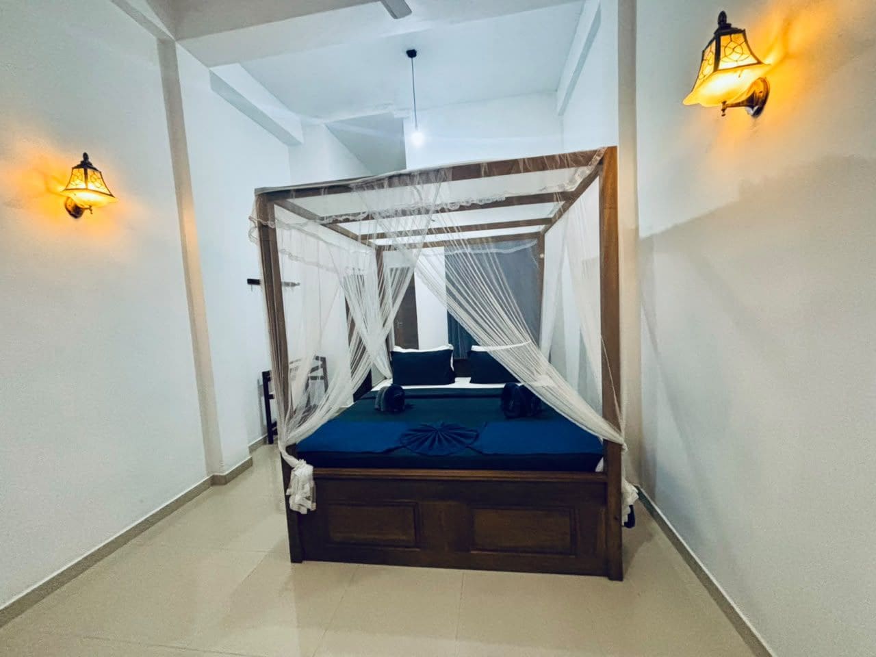 A room with a bed under a canopy, two wall-mounted lights, and a ceiling fan.