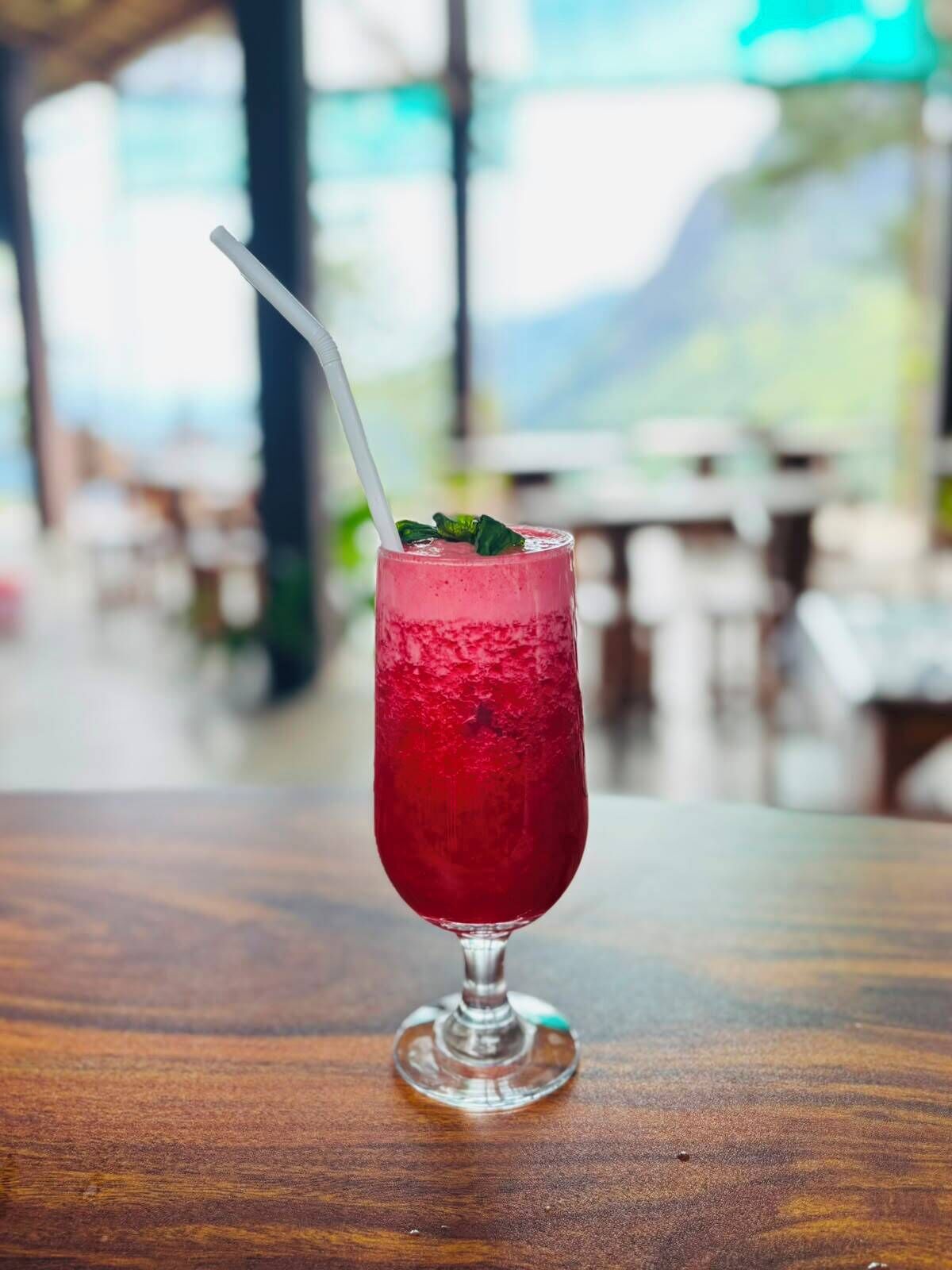 A glass of red beverage on a wooden table with a blurred background of a restaurant or cafe.