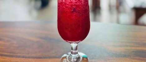 Un vaso de bebida roja sobre una mesa de madera, con un fondo borroso de un restaurante o cafetería.