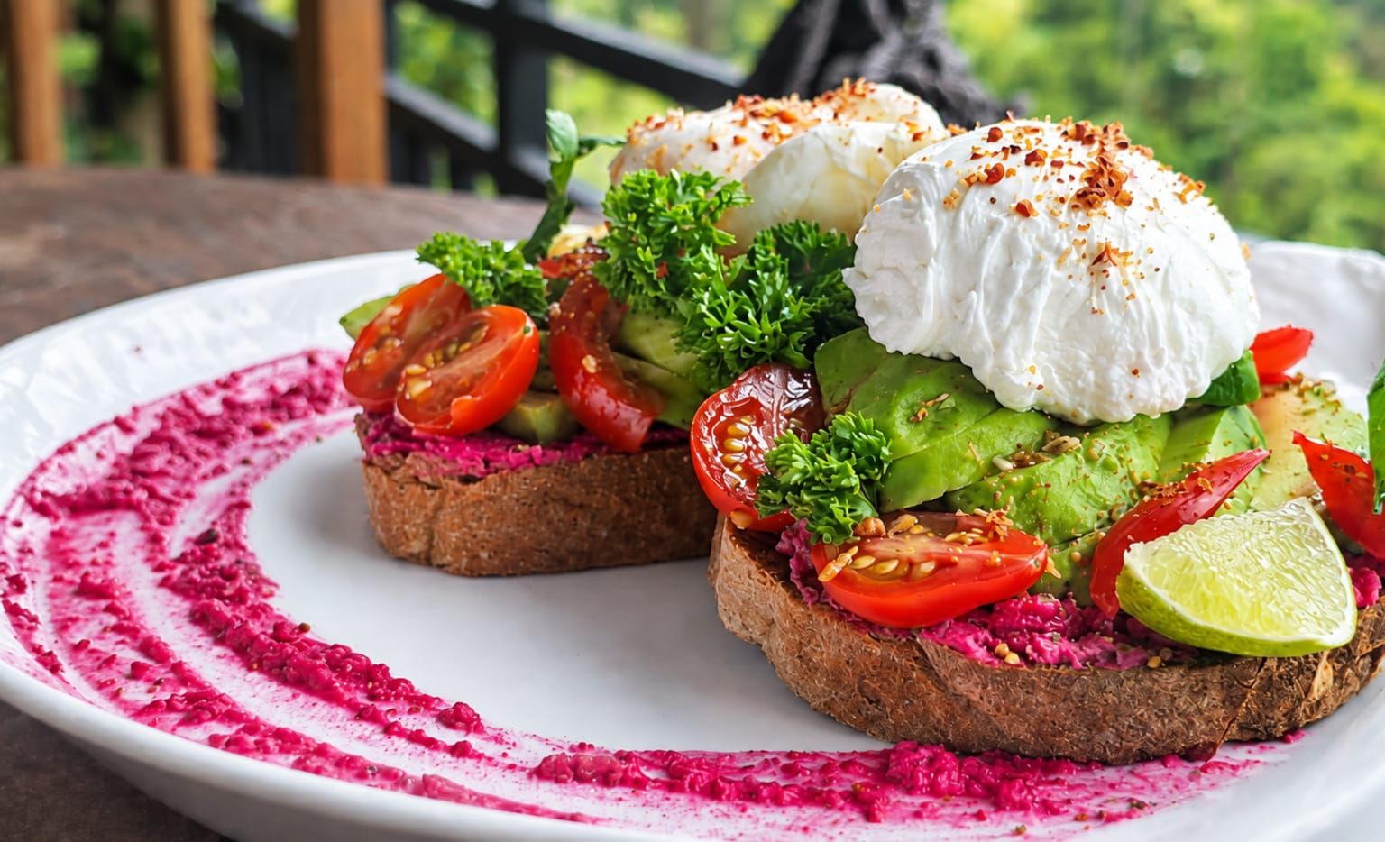 Two open-faced sandwiches with various toppings on a white plate, set on a wooden table.