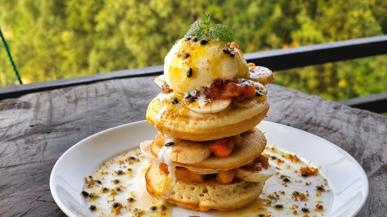 Una pila de tortitas con un huevo pochado encima, adornadas con hierbas, servidas en un plato blanco.