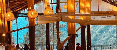 Un intérieur agrémenté de poutres en bois, de luminaires suspendus et de tables avec des chaises.