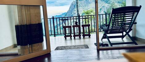A balcony with a view of mountains, a wooden table, and a black chair.