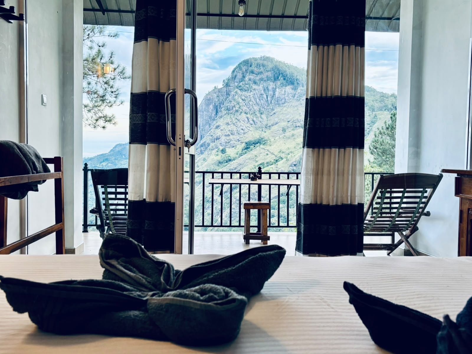 A room with a bed, two chairs, a small table, and a balcony with a mountain view.