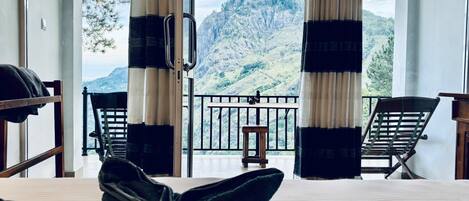A room with a bed, two chairs, a small table, and a balcony with a mountain view.