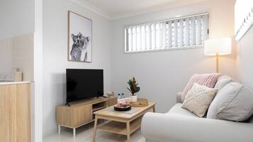 Una sala de estar moderna con un televisor de pantalla plana, una mesa de centro de madera, un sofá blanco y una ventana con persianas.