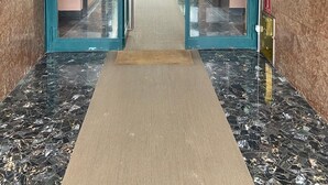 L’entrée d’un hôtel, avec une porte en verre, un tapis et un sol en marbre.