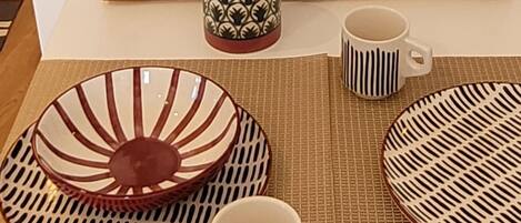 Ein Esstisch-Set mit einer gemusterten Schüssel, einer Tasse und einem Untertasse auf einer gewebten Tischunterlage.