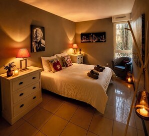 A bedroom with a bed, bedside tables, a chair, a window, and a painting on the wall.