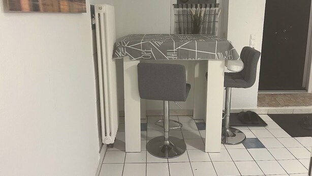 A compact room with a dining table, two chairs, a radiator, a door, and a window with curtains. - Small but nice in Nöpke. (Nöpke)