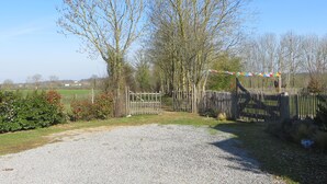 Une allée de gravier mène à un portail en bois, qui est lui-même bordé d’une clôture et d’arbres.