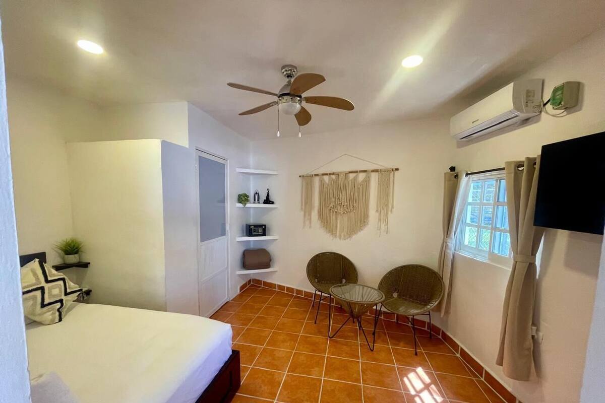 A bedroom with a bed, a ceiling fan, a TV, a window with curtains, and a small table with chairs.