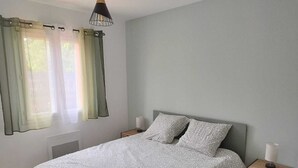 Et soveværelse med en seng, to sengeborde, et vindue med gardiner og en hængende lampe.