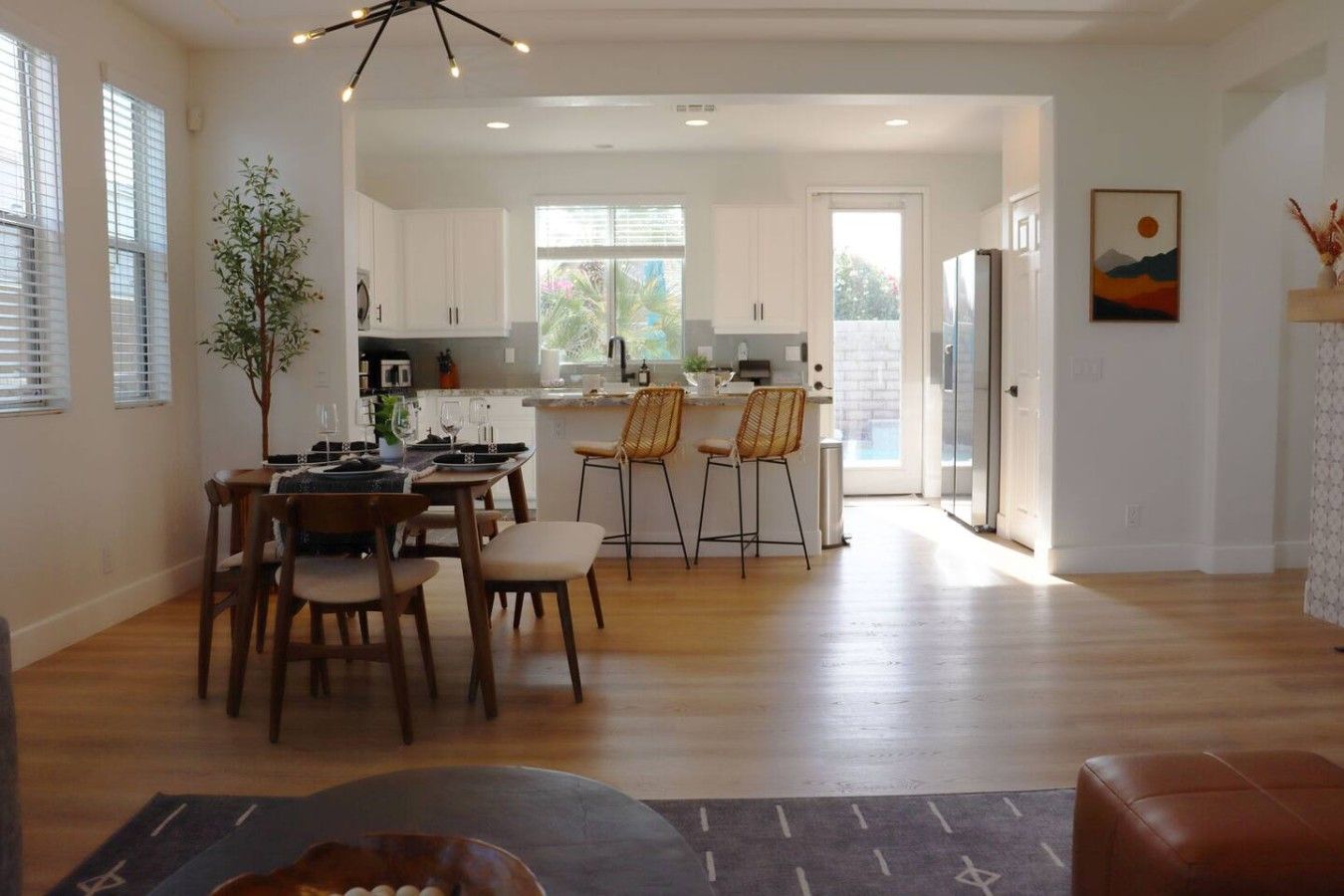 A spacious kitchen with white cabinets, a dining area with wooden chairs, and a view of the outdoors through large windows.