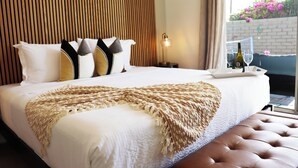 Una cama bien hecha con un plaid con forma de corazón, un cabecero de madera y una mesita de noche con una lámpara.