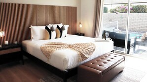 Un dormitorio moderno con una cama grande, cabecera de madera, mesita de noche con lámpara y vistas al exterior.