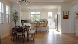 Una cocina moderna con armarios blancos, un comedor con sillas de madera y un amplio ventanal que proporciona luz natural.