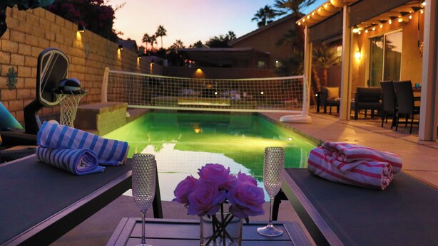 Escena junto a la piscina con una zona protegida por mosquiteras, sillas de descanso y una mesa con un jarrón de flores.
